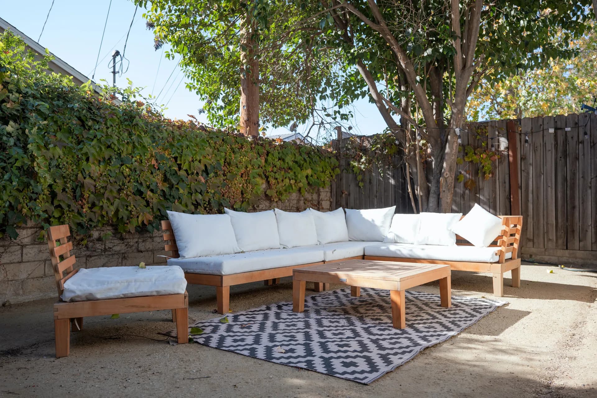 Cushioned wooden corner sofa and coffee table under mature trees