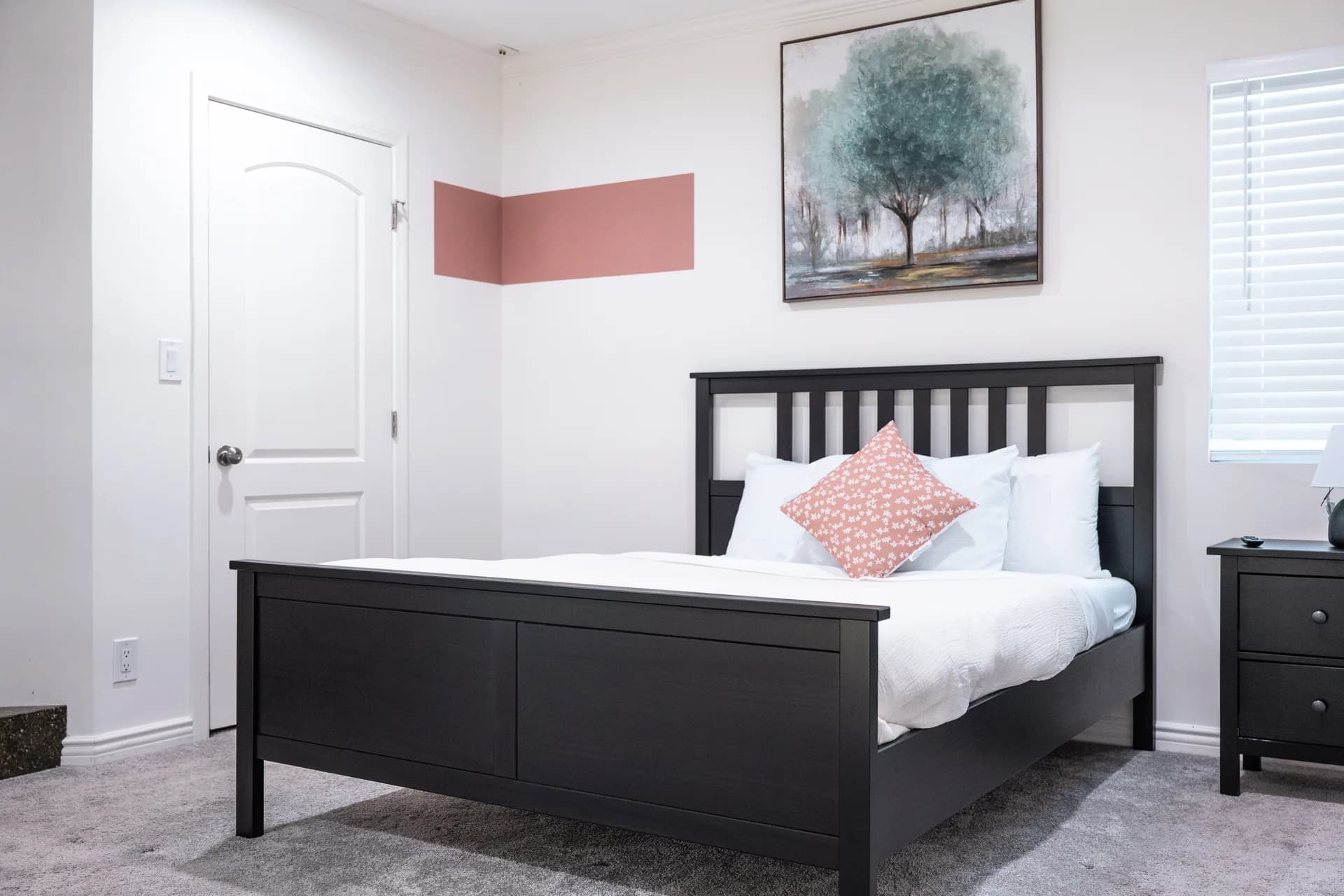 Bedroom with a dark wood bed, white linens, and a blush accent wall