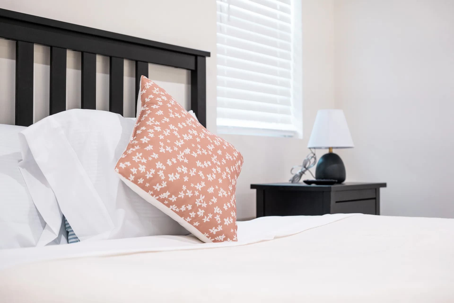 White pillows and a blush patterned cushion against a dark wooden headboard