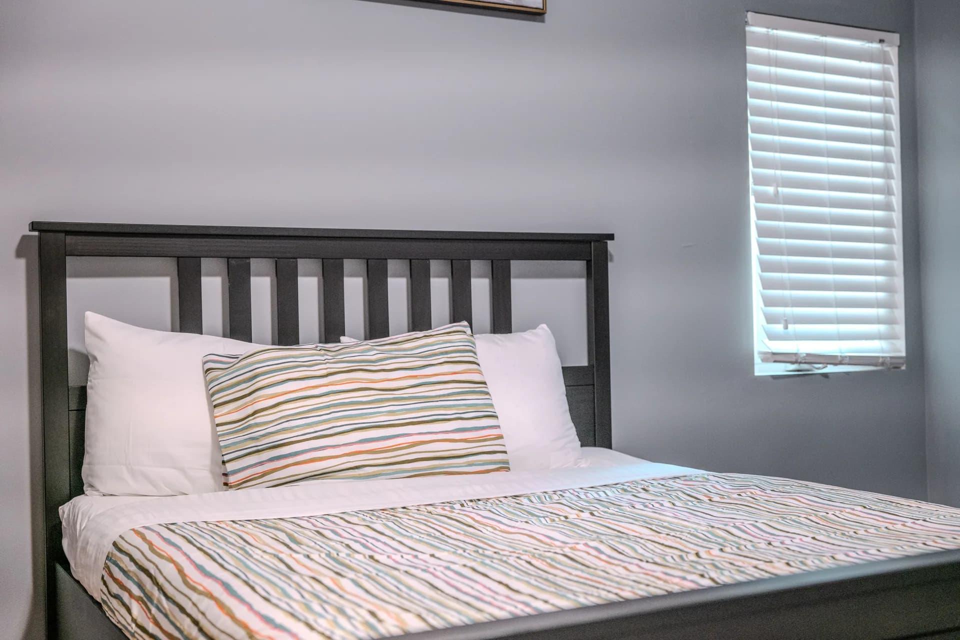 Dark wood bed with striped bedding against a grey wall